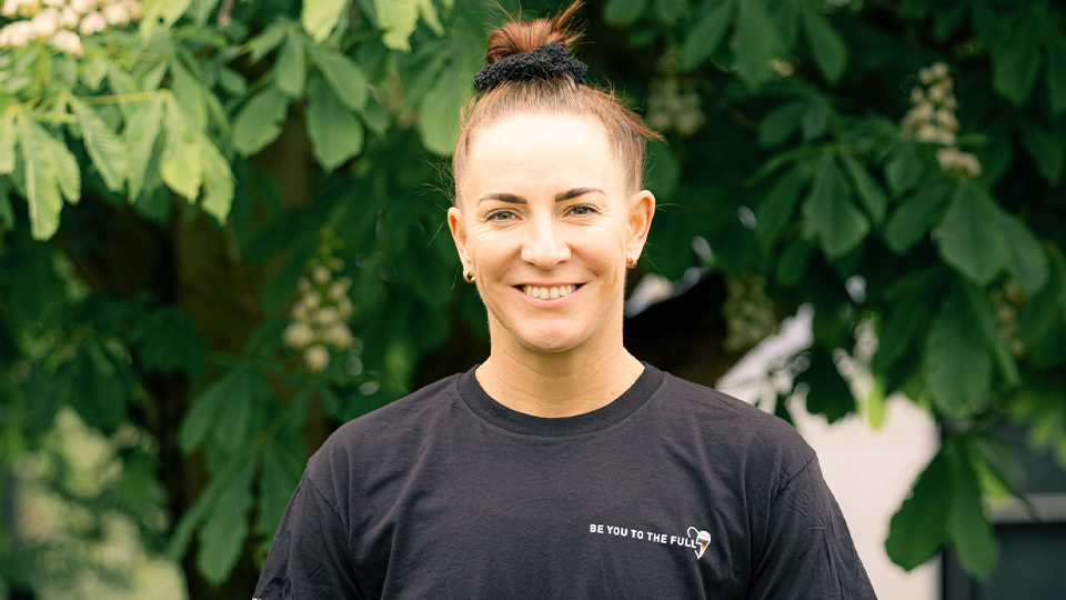 shadine van der merwe stood smiling with the limited edition pride tshirt on